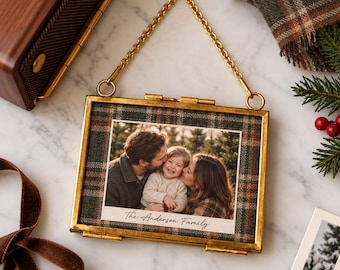 Könnte beinhalten: Ein rechteckiger Bilderrahmen aus Messing zum Aufhängen mit einem Rand aus Schottenkaro-Stoff. In der Mitte befindet sich ein Familienfoto mit dem Schriftzug The Anderson Family in Schreibschrift unten. Eine goldene Kette ist befestigt.