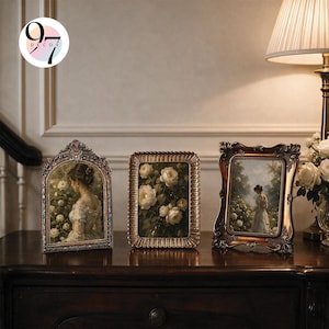 Three vintage picture frames resting on a dark wooden console table next to a lamp and white flowers.