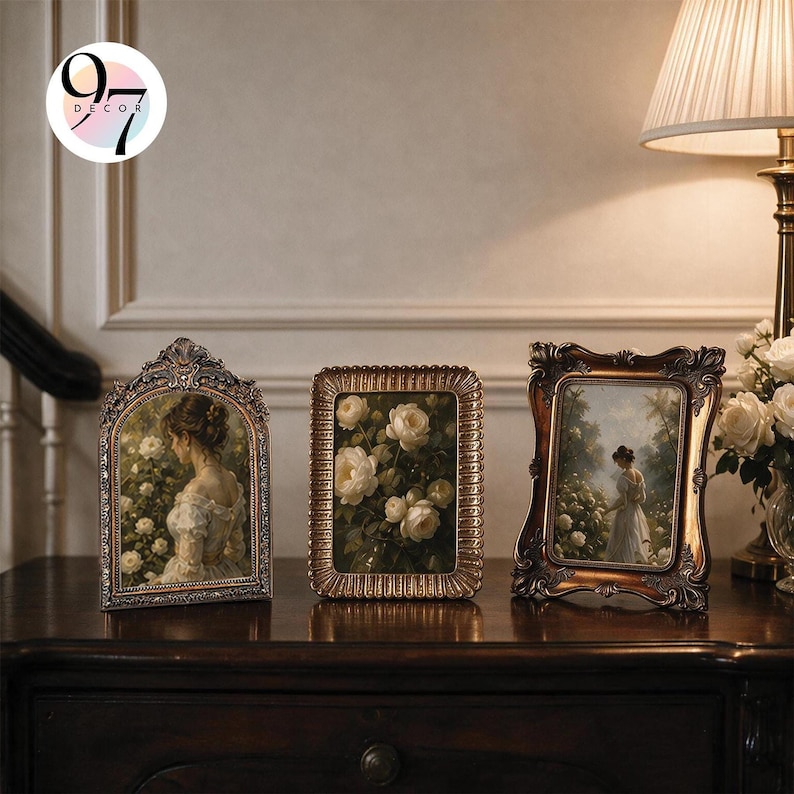 Three vintage picture frames resting on a dark wooden console table next to a lamp and white flowers.