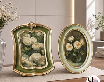 May include: Two decorative picture frames featuring floral artwork. The left frame is rectangular with a scalloped edge, finished in dark green and gold. The right frame is oval, finished in light green and gold. Both contain paintings of white roses.