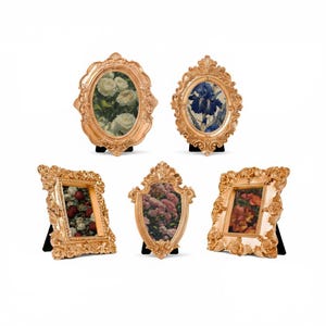 May include: Set of five ornate gold-colored picture frames in various shapes, including oval, rectangular, and shield. Each frame holds a floral print and stands on a black easel.