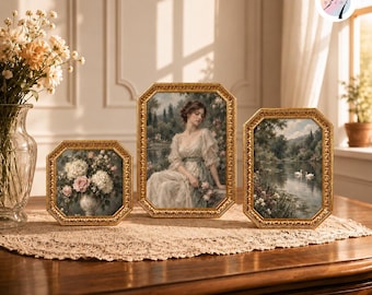 Könnte beinhalten: Drei achteckige goldfarbene Rahmen mit Kunstdrucken. Der linke Rahmen zeigt einen Blumenstrauß, der mittlere Rahmen eine Person in einem hellen Kleid und der rechte Rahmen eine Landschaft mit zwei weißen Schwänen auf einem ruhigen See.