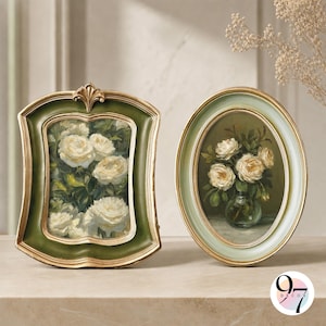 May include: Two decorative frames with floral artwork. The left frame is rectangular with a dark green border and gold trim, displaying white roses. The right frame is oval with a light green border and gold trim, showing white roses in a vase.