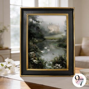 May include: A rectangular wall art print in a black frame with gold inner trim, depicting a misty landscape with a large house, a calm river, and three white swans swimming among green foliage and small white flowers in the foreground.