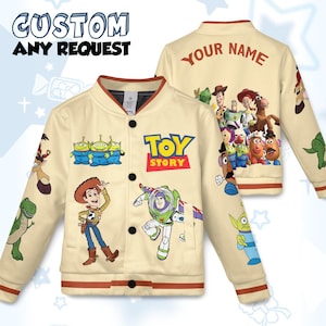 Puede incluir: Chaqueta bomber color crema con personajes de la película animada "Toy Story". La chaqueta tiene cierres de botón a presión negros, un cuello marrón y las palabras "CUSTOM ANY REQUEST" y "YOUR NAME" impresas. La parte delantera muestra el logotipo de "Toy Story".
