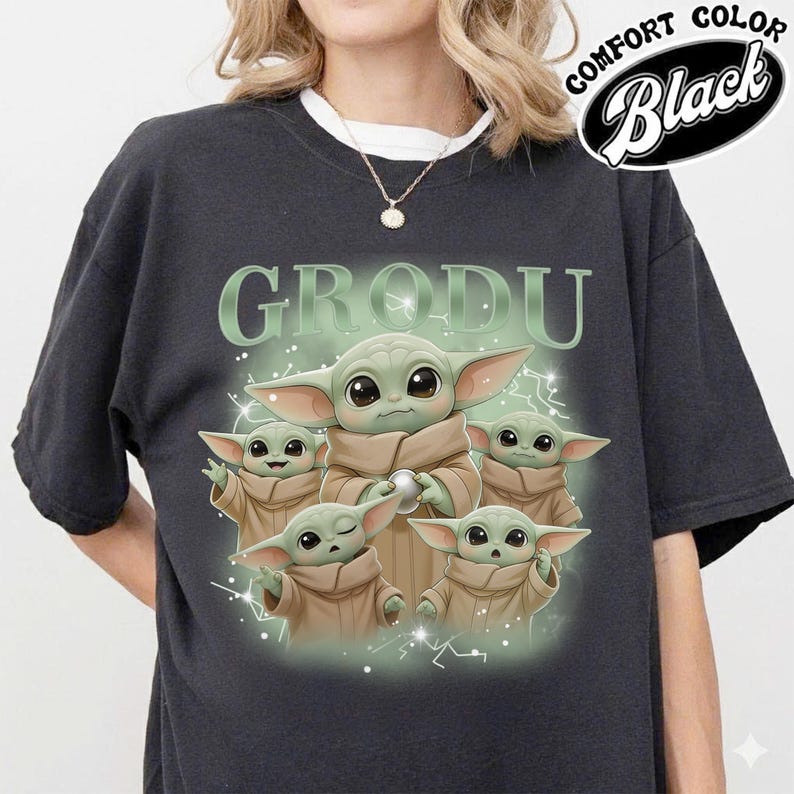 May include: Black comfort color t-shirt featuring a graphic of Grogu, the character from The Mandalorian, with the word "GRODU" above. The design shows Grogu in various poses with a light green and white color scheme.