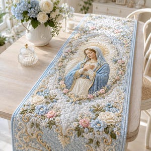 May include: A rectangular quilted table runner featuring a central embroidered depiction of a figure in a blue and white robe with hands crossed over the chest, surrounded by intricate floral patterns in shades of blue, pink, and cream.