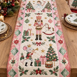 May include: A quilted Christmas table runner featuring a cream-colored center with embroidered nutcracker, mouse, and ballerina figures, surrounded by a pink and green diamond-patterned border decorated with poinsettias and snowflakes.