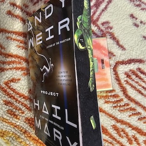 May include: A hardcover book titled "Project Hail Mary" by Andy Weir. The cover features an astronaut and the text "Soon to be a major motion picture starring Ryan Gosling". The book is a New York Times bestseller.