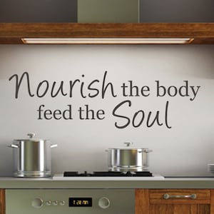 May include: A kitchen with a white wall and a wooden cabinet above the stove. The wall has a black vinyl decal with the text "Nourish the body feed the Soul".