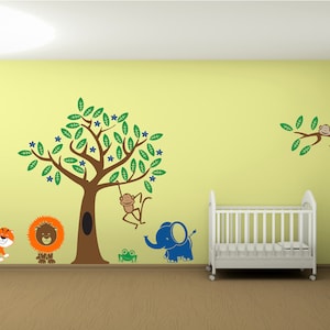 May include: A nursery wall decal set featuring a green tree with blue flowers, a brown monkey hanging from a branch, a blue elephant, a green frog, a brown lion, and an orange tiger. The decals are on a yellow wall with a white cot in the background.