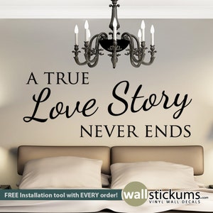 May include: A black and white vinyl wall decal with the text "A TRUE Love Story NEVER ENDS". The decal is displayed on a wall in a bedroom with a bed and a chandelier.