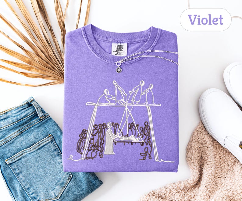 May include: A violet Comfort Colors sweatshirt with an embroidered design of figures on a swing set. The sweatshirt is paired with blue jeans, white sneakers, and a necklace. The word "Violet" is displayed in a white oval.