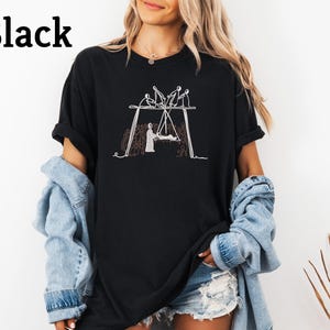 May include: Black t-shirt with a white line drawing of a swing set with figures. The word "Black" is printed in large, bold, black letters at the top left of the shirt. The shirt is a casual, oversized style.