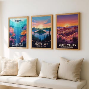Op de afbeelding: Drie ingelijste kunstdrukken met landschappen van nationale parken. De prints tonen Biscayne, Crater Lake en Death Valley. Elke print heeft een houten lijst en toont levendige kleuren, waaronder blauw, oranje en paars. De tekst "Biscayne National Park", "Crater Lake National Park" en "Death Valley National Park" is zichtbaar.