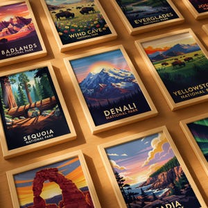 Op de afbeelding: Een verzameling ingelijste kunstprints met landschappen van nationale parken. Elke print heeft een houten lijst en toont levendige illustraties van locaties zoals Denali, Yellowstone en Badlands National Park. De prints zijn gerangschikt op een lichtgekleurd houten oppervlak.
