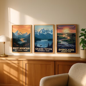 Op de afbeelding: Drie ingelijste kunstprints met landschappen van nationale parken. De prints tonen de Rocky Mountains, Grand Teton en Everglades. Elke print heeft een houten lijst en de naam van het park. De kleurenpaletten omvatten oranje, blauw en groen.