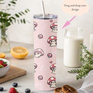 May include: A pink insulated tumbler with a repeating pattern of cartoon mushrooms and hearts. The tumbler has a silver lid and a white straw. The design is set against a light pink background with small white dots.