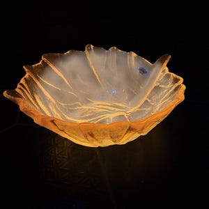 Op de afbeelding: Een doorschijnende, amberkleurige glazen schaal met een geschulpte, bladachtige rand. De binnenzijde heeft een matte, witachtige afwerking met zichtbare goudgele nerven die de organische textuur van een natuurlijk blad nabootsen.