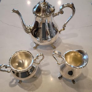 May include: A set of three ceramic mugs with a speckled, matte finish. The mugs are in shades of cream, light gray, and dark gray. Each mug has a simple, minimalist design and a rounded handle. The mugs are likely for coffee or tea.