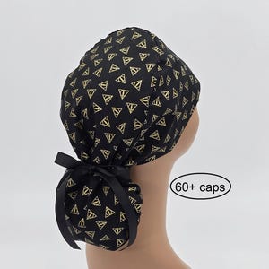 May include: Black surgical cap with a gold geometric pattern. The cap is tied in the back with a black ribbon. The text "60+ caps" is in a white oval.