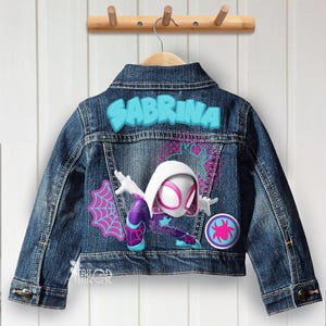 May include: A blue denim jacket with the name "SABRINA" in turquoise letters across the back. The jacket features a Spider-Gwen graphic with pink and purple accents. A round patch with a spider logo is also visible.