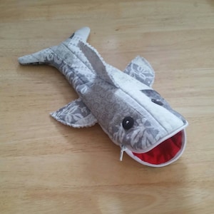 May include: A gray and white fabric shark pencil case with a red zippered mouth and black eyes.