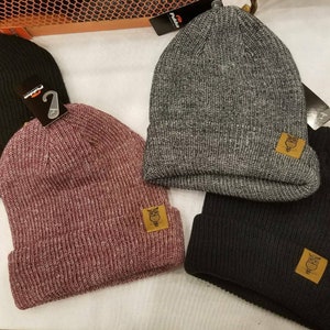 May include: Three knit beanies in different colors: burgundy, gray, and black. Each beanie has a small brown patch with an owl design on the front.