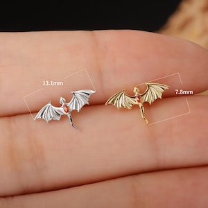 May include: Two dragon-shaped earrings. One is silver-colored, the other is gold-colored. Each dragon has outstretched wings and a red gemstone. The silver dragon measures 0.5 inches long. The gold dragon measures 0.3 inches long.