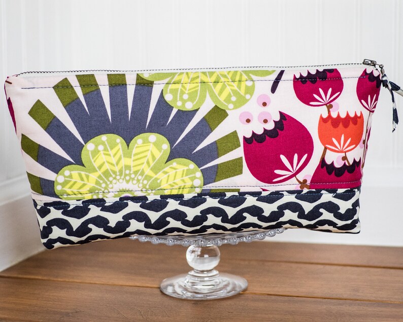 May include: A pink, green, and red floral print zippered pouch with a black and white geometric pattern on the bottom.