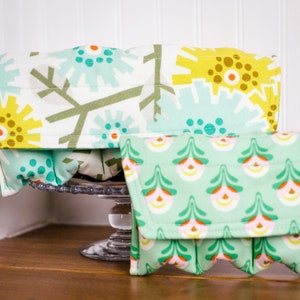 May include: Two fabric storage containers with a green and yellow floral pattern. The larger container is open and the smaller container is closed.