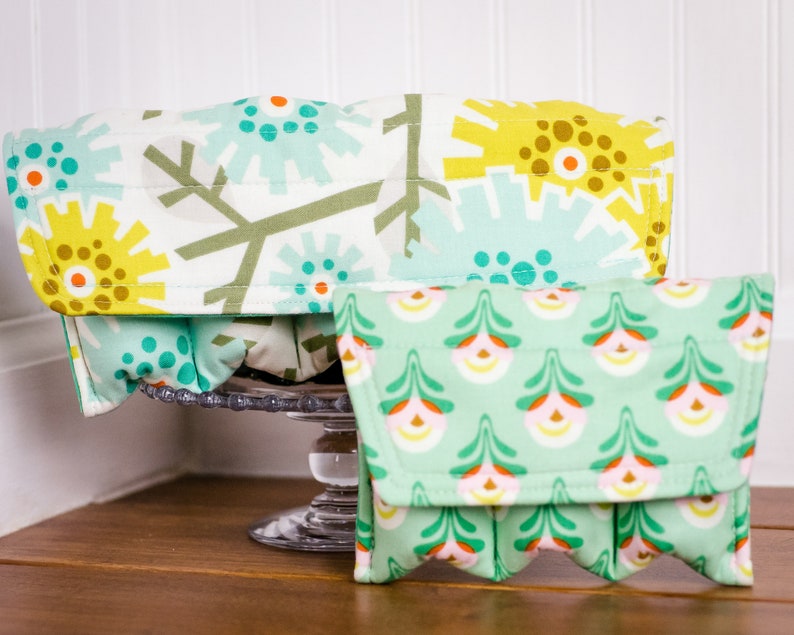 May include: Two fabric storage containers with a green and yellow floral pattern. The larger container is open and the smaller container is closed.