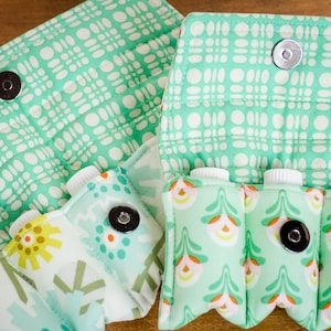 May include: A green fabric pouch with four pockets for holding small bottles. The pouch has a snap closure and a floral pattern.