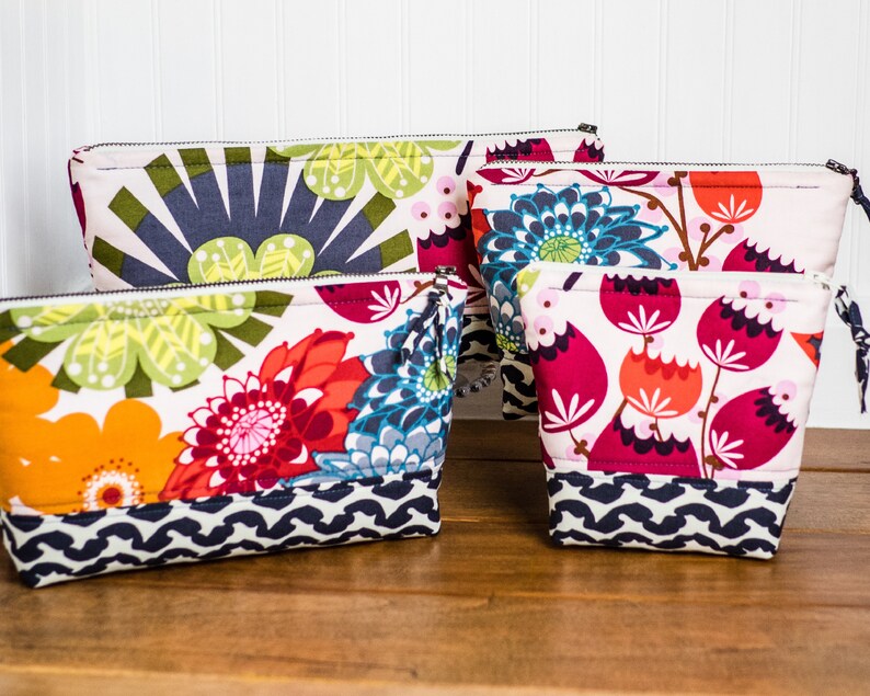 May include: Four different sized zippered pouches with floral patterns. The pouches are made of fabric and have a white background with colorful flowers. The pouches are lined with a black and white geometric pattern.