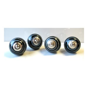 May include: Four black and silver ceramic cabinet knobs with a glossy finish. Each knob features a silver floral design in the center and is accented with silver and black stripes. These decorative knobs are ideal for adding a touch of elegance to furniture.