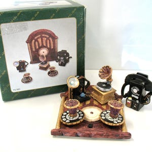 May include: A miniature tea set featuring a brown radio-shaped tray, two telephone-shaped teapots, a gramophone-shaped teapot, and two cup-shaped pieces with rotary dial patterns. The set is displayed with its original green cardboard box labeled TS 593.