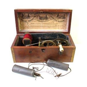 May include: Antique wooden Davis & Kidder's Patent Magneto-Electric Machine, open to reveal internal gears, a red spool, and two cylindrical batteries. The lid features an illustrated advertisement for nervous disease treatment.
