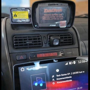 May include: Car dashboard featuring a FuelTech display and a digital screen. The FuelTech display has text in English, Spanish, and Portuguese. The digital screen shows music details and the time, 12:58 PM.
