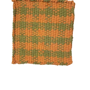 May include: A square, woven potholder with a repeating pattern of orange and olive green. The edges are finished with a twisted orange border. The potholder is designed for kitchen use.