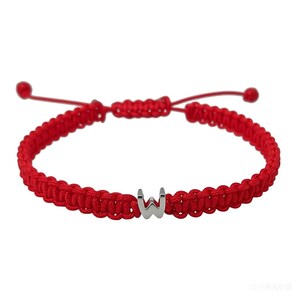 May include: Red braided bracelet featuring a silver letter "W" charm. The bracelet is adjustable with sliding knots and red cord. A simple and stylish accessory.