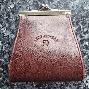 May include: A dark brown coin purse with a textured surface and a silver-toned metal kiss-lock clasp. The front of the purse features the embossed text "RICH ARD-DAY" and the initials "RD" centered below the text in a clear, legible font.