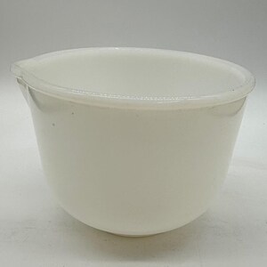 May include: A solid white mixing bowl made of opaque glass. The bowl features a smooth, rounded body with a distinct pouring spout integrated into the rim. The interior and exterior surfaces are uniform in color, showing a clean, simple design.
