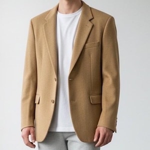 Peut inclure: Un blazer beige à deux boutons, avec un revers cranté et deux poches avant. Le blazer est porté sur un t-shirt blanc et associé à un pantalon gris. L'ensemble est de style classique et élégant.