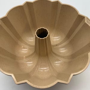 May include: Tan bundt cake pan with a fluted design. The pan has a central tube and a scalloped edge. The interior has a non-stick surface. This baking pan is perfect for making cakes and other baked goods.