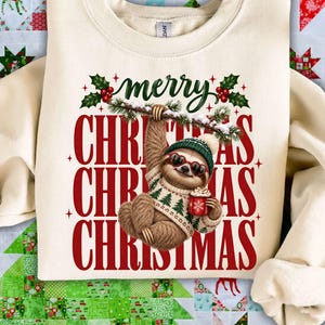 Könnte beinhalten: Ein cremefarbenes Sweatshirt mit Rundhalsausschnitt und einem Aufdruck eines Faultiers, das eine herzförmige Sonnenbrille und einen grünen Strickpullover trägt. Das Faultier hält eine rote Tasse und hängt an einem verschneiten Ast. Text: merry CHRISTMAS CHRISTMAS CHRISTMAS.