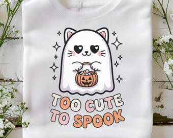 May include: A white crewneck sweatshirt featuring a graphic of a white ghost cat with heart-shaped eyes holding an orange jack-o'-lantern candy bucket. The text below the graphic reads "TOO CUTE TO SPOOK" in a rounded, multi-colored font.