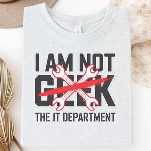 May include: Light gray t-shirt with the text "I AM NOT GEEK THE IT DEPARTMENT". The word "GEEK" is crossed out with a red line, and two crossed wrenches are in the center.
