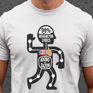 Puede incluir: Camiseta blanca con un gráfico negro de un hombre de palo. El gráfico incluye el texto "99% Reggaeton Lyrics" y "Adobo & Sazón", junto con la bandera de Puerto Rico.