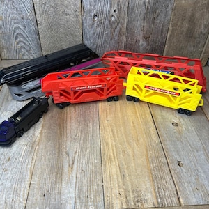 May include: A collection of Micro Machines toy train cars including a black engine, a long black car, a red car, and a yellow car. Each car features a lattice-style frame and the text Micro Express printed on the side in a rectangular label.