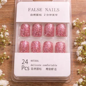 May include: A pack of 24 false nails with a shimmering pink finish. The packaging features the text "FALSE NAILS" and Chinese characters. The nails are described as natural, delicate, and comfortable.